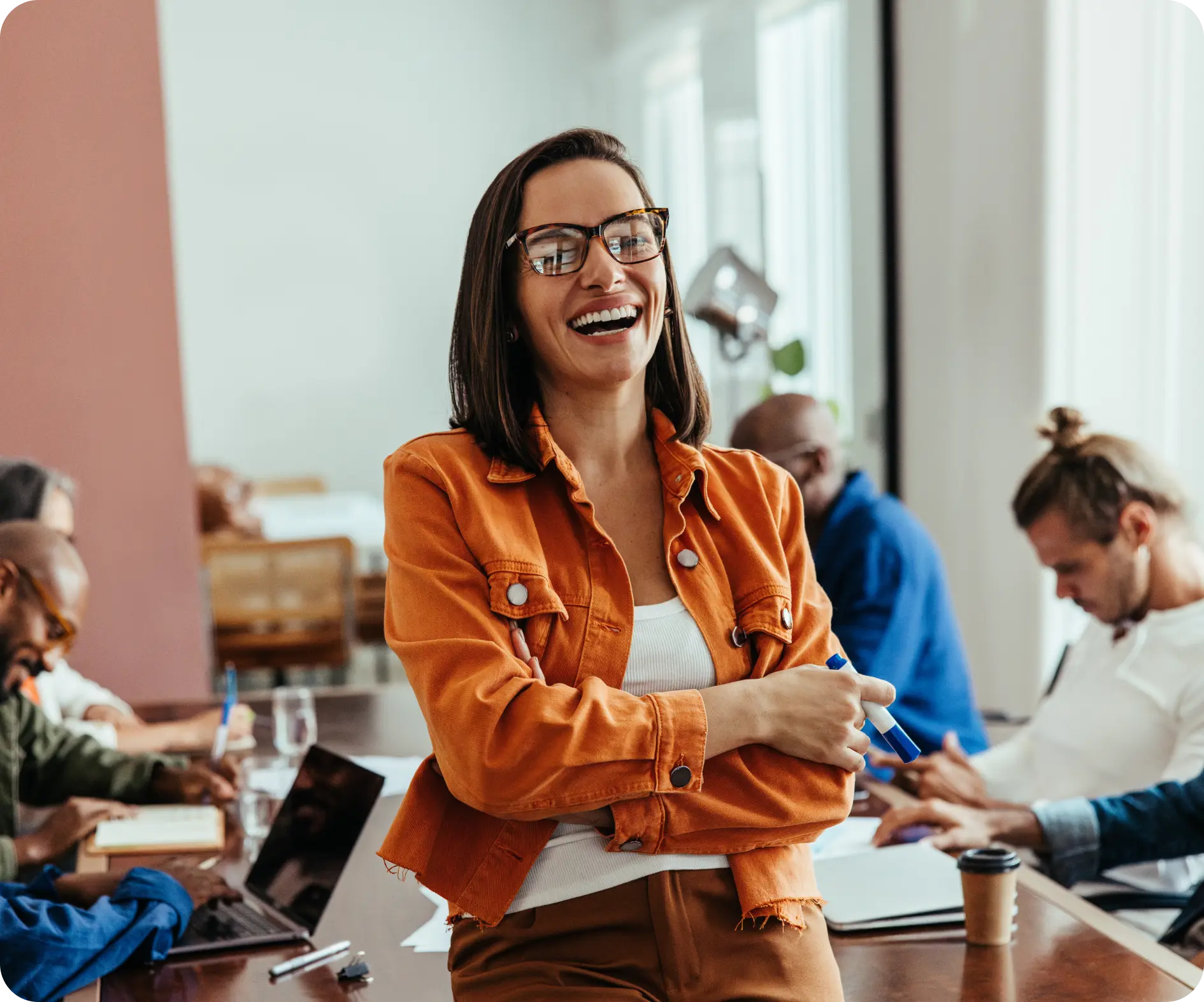 A woman with glasses smiles while seated at a conference table, reflecting a positive and collaborative atmosphere.