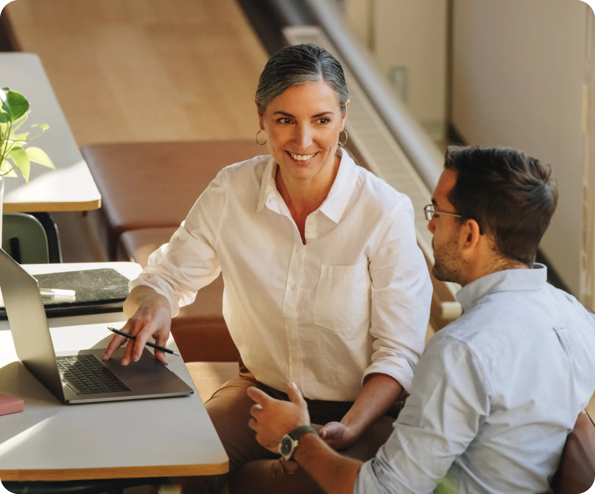 A man and woman are seated at a table, engaged with a laptop in front of them, discussing or collaborating on a project.